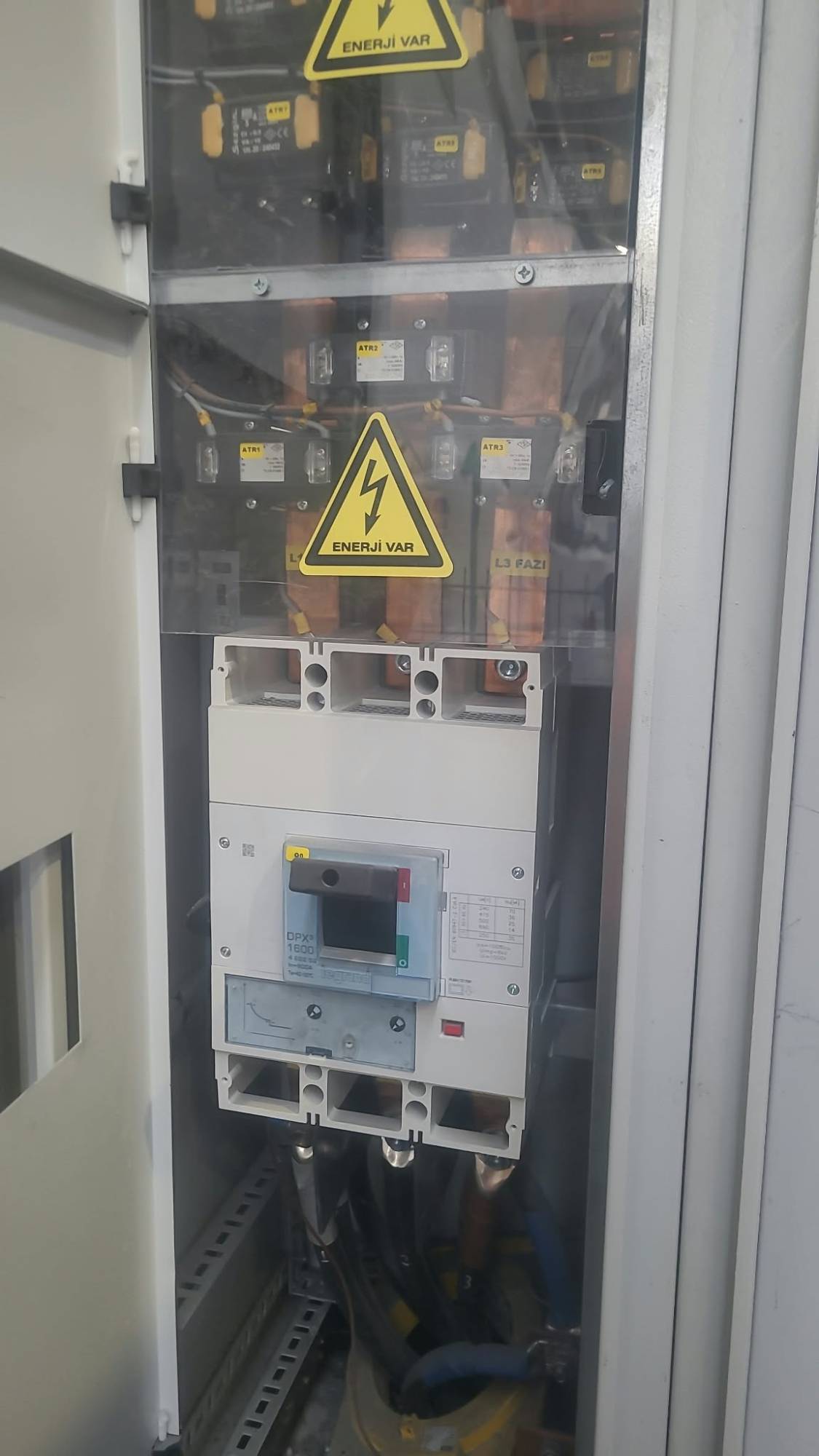 Kompakt güç şalteri (MCCB) bölmesi; bara bağlantıları ve 'Enerji Var' uyarı etiketi.